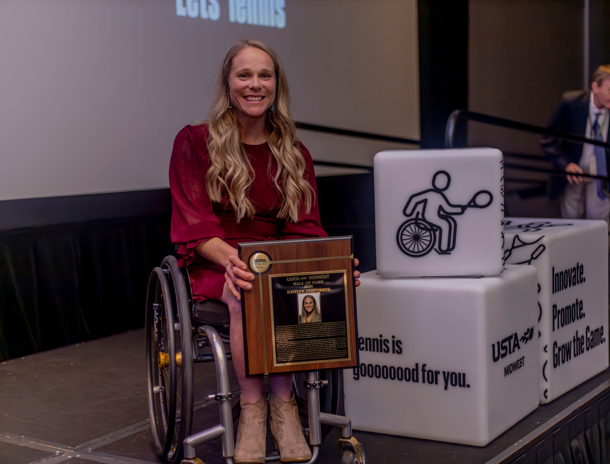 Kaitlyn Verfuerth smiling on stage with her USTA Midwest Hall of Fame plaque.